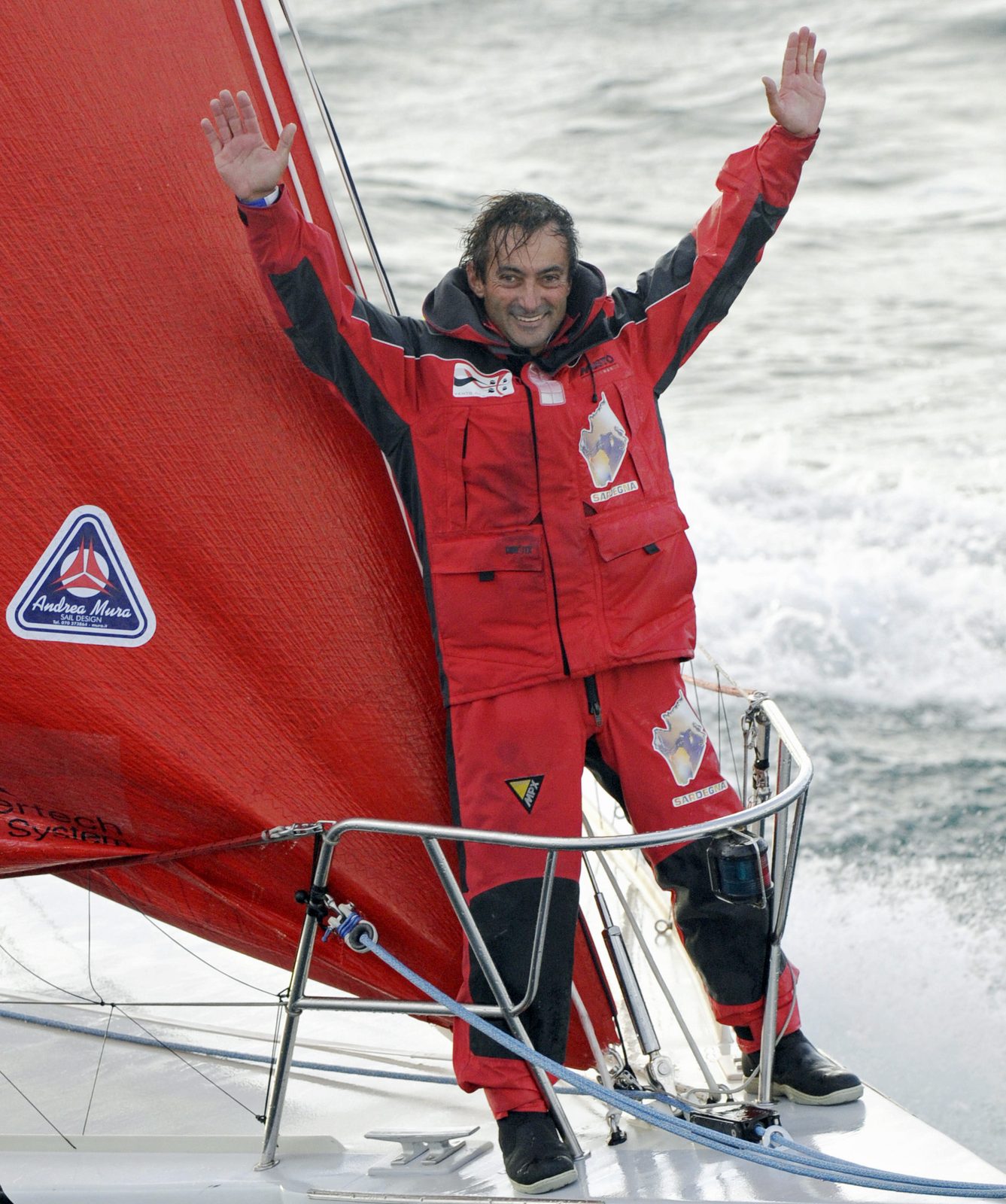 Andrea Mura in cerata rossa saluta a braccia alzate dalla prua